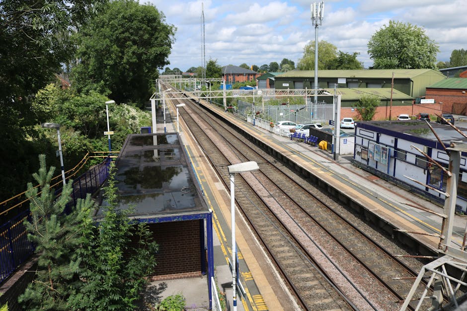 A busy railway yard with multiple parallel train tracks, some with modern yellow and grey commuter trains, parked and ready for departure. The tracks are made of steel rails set on wooden sleepers, wi